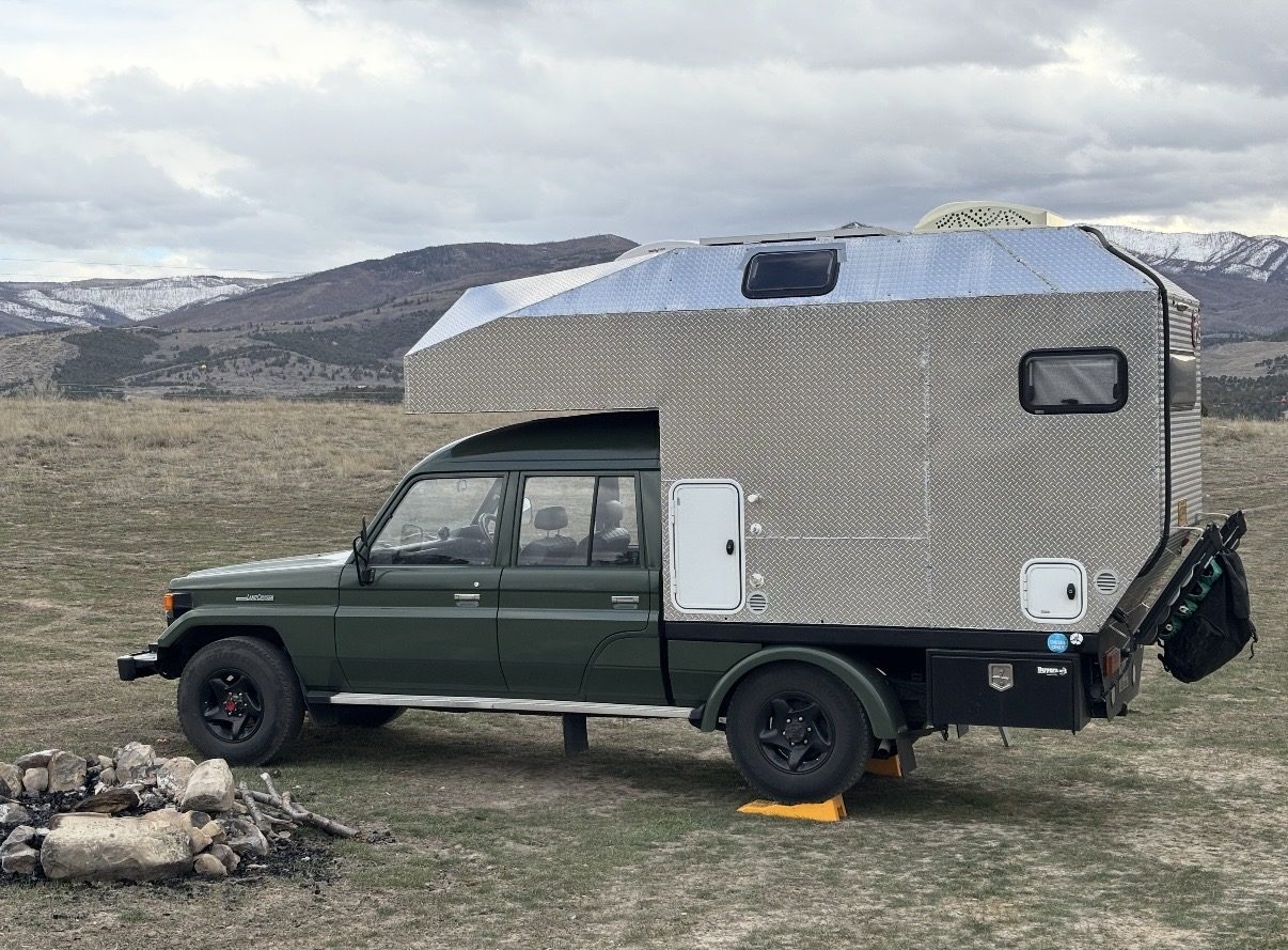 Side view of KENDL showing its aluminum diamond-plate body, white entry door, storage compartments and mounting on the green Land Cruiser